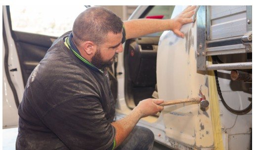 Panel beater repairing a vehicle door panel by hand